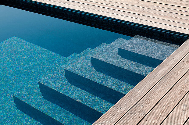 Eine Treppe führt in ein klares blaues Schwimmbecken. Der Pool ist von einem Holzdeck umgeben. 
