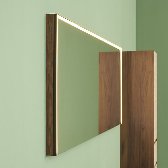 Ein rechteckiger Wandspiegel mit einem Holzrahmen und eingebauter LED-Beleuchtung entlang des Randes.