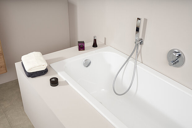 Moderne weiße Badewanne mit verchromtem Wasserhahn und Handbrause in einem minimalistischen Badezimmer. 