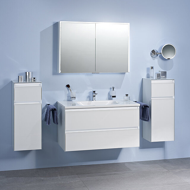 Ein Badezimmer mit hellblauen Wänden, einem an der Wand montierten Waschbecken, zwei weißen Schränken auf beiden Seiten und einem Spiegelschrank.