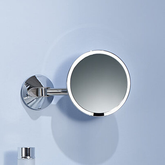 Ein runder Kosmetikspiegel mit Metallrahmen und -arm ist an einer Wand befestigt.