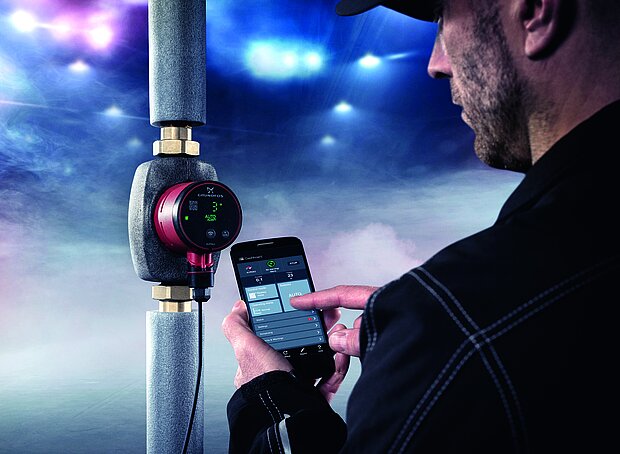 Ein Mann verwendet ein Smartphone, um ein rotes elektronisches Gerät zu steuern oder zu überwachen, das an einem isolierten Rohr befestigt ist.