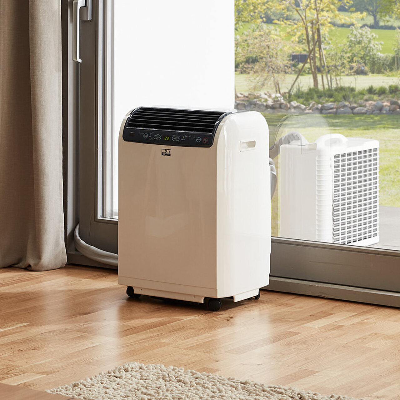 [Translate to Italienisch:] Ein Wohnzimmer mit einem beigen Sofa und Kissen, einer Stehlampe, einem kleinen Tisch und einer mobilen Klimaanlage.