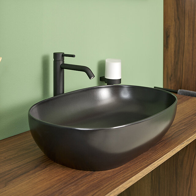 Ein modernes, mattschwarzes, ovales Waschbecken mit einem passenden schwarzen Wasserhahn steht auf einer hölzernen Arbeitsplatte.