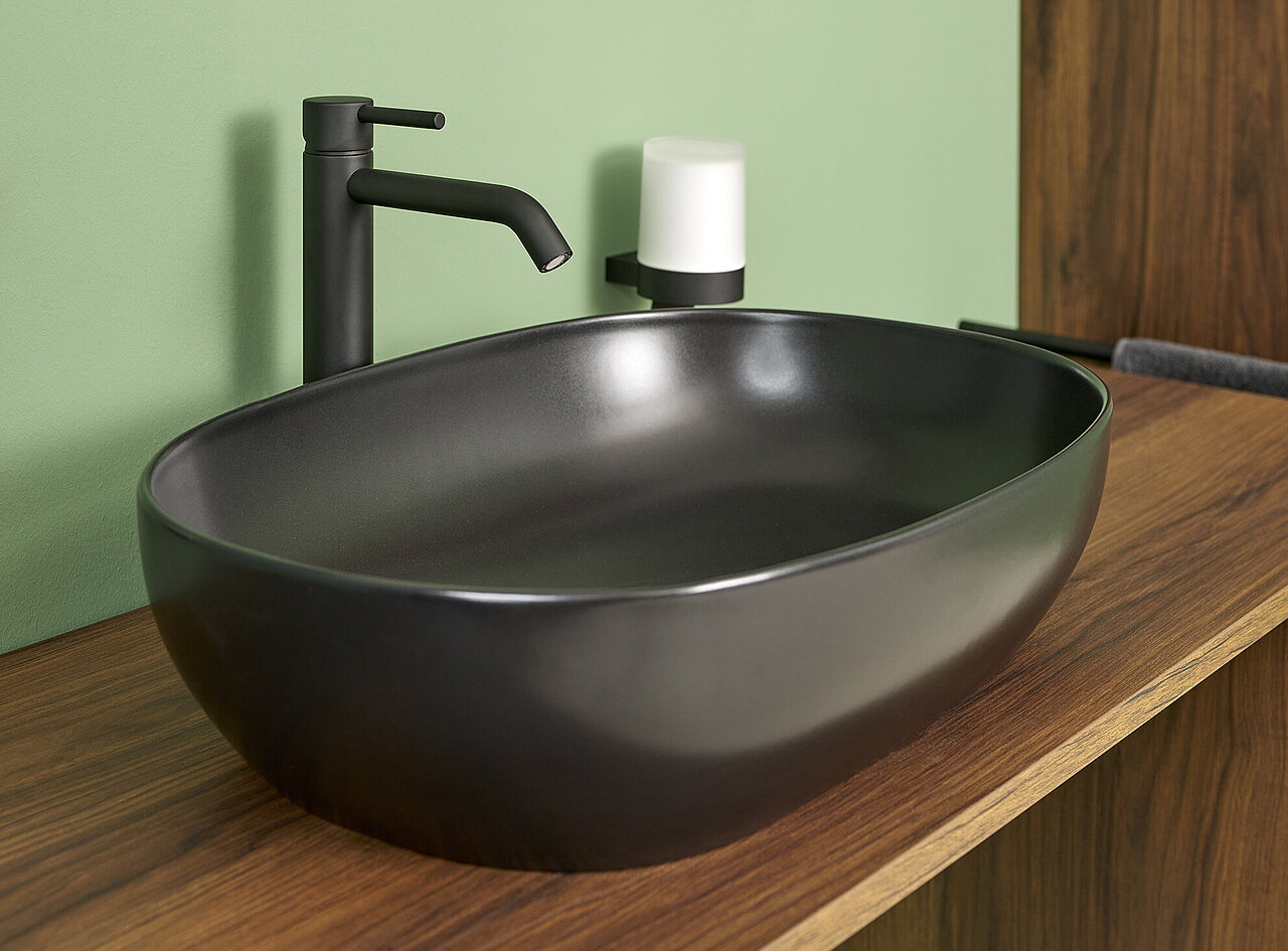 Ein modernes, mattschwarzes, ovales Waschbecken mit einem passenden schwarzen Wasserhahn steht auf einer hölzernen Arbeitsplatte.