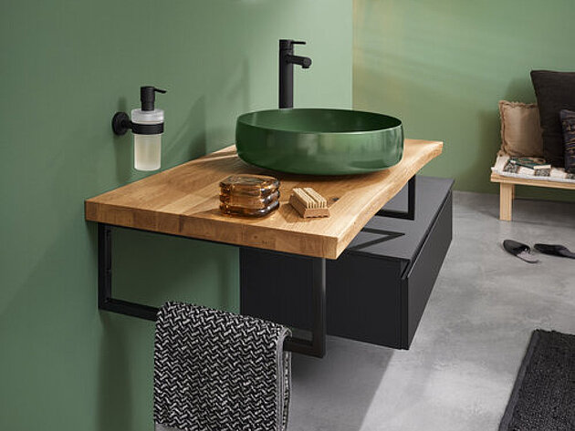 Ein moderner Waschtisch mit einer Arbeitsplatte aus Holz, einem grünen Waschbecken, einem schwarzen Wasserhahn.