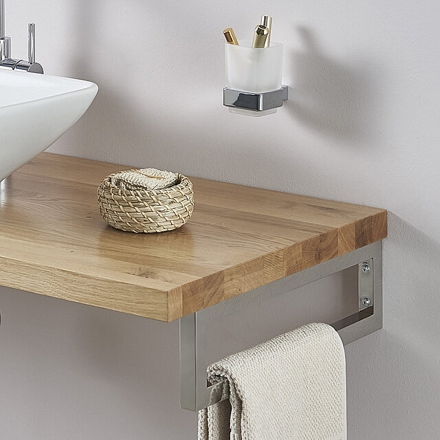 Ein moderner Badezimmertisch mit einer Holzoberfläche, einem geflochtenen Korb und einem an einer Metallstange hängenden Handtuch.