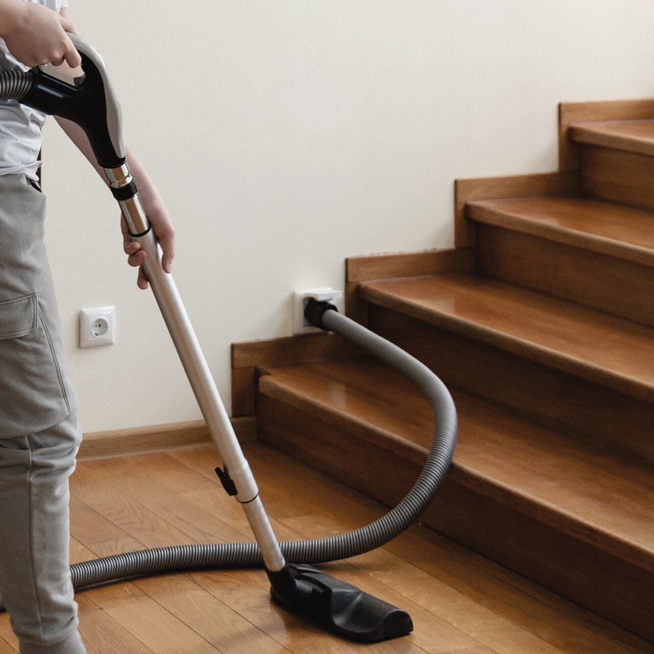 Person saugt Holztreppe mit Schlauch; Anschluss an zentrale Staubsaugeranlage neben der Treppe.