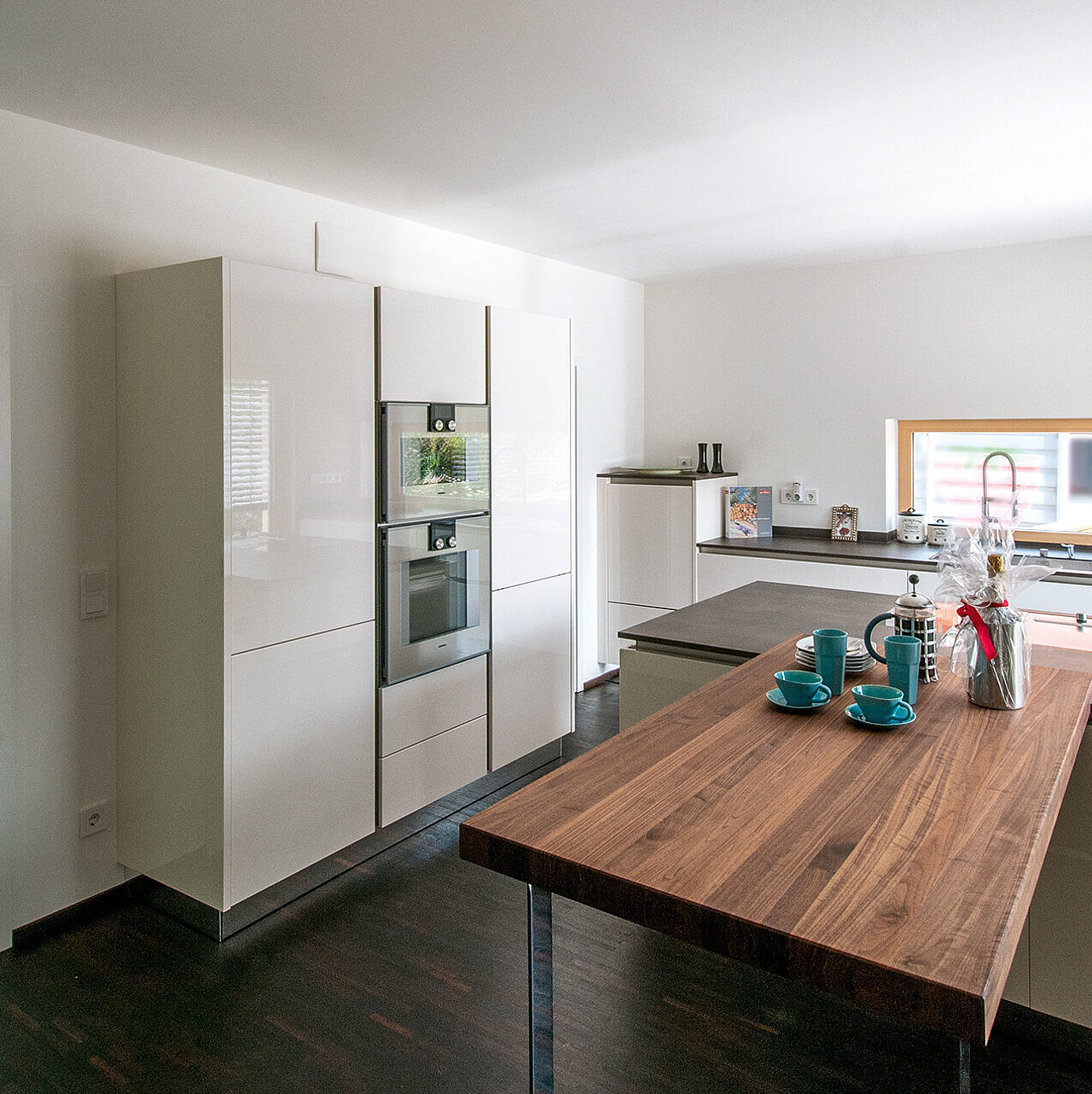 Moderne Küche mit hellen Wänden, einer großen Holzinsel, Einbaugeräten und einem Fenster über der Spüle.