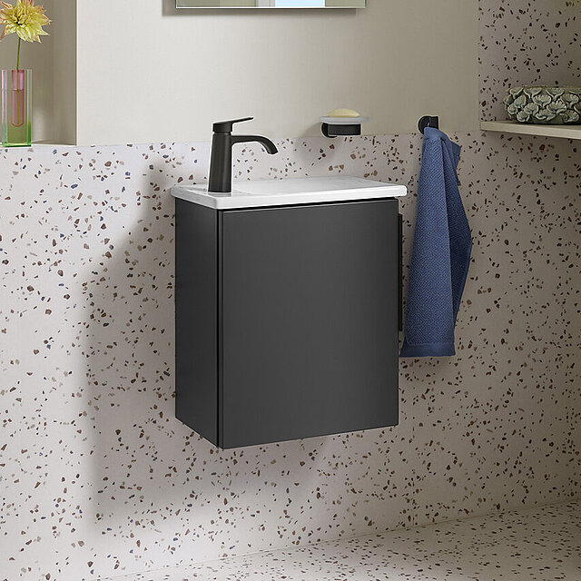 Badezimmer mit Terrazzoböden und -wänden, einem schwarzen Waschbeckenschrank und einem großen Spiegel.