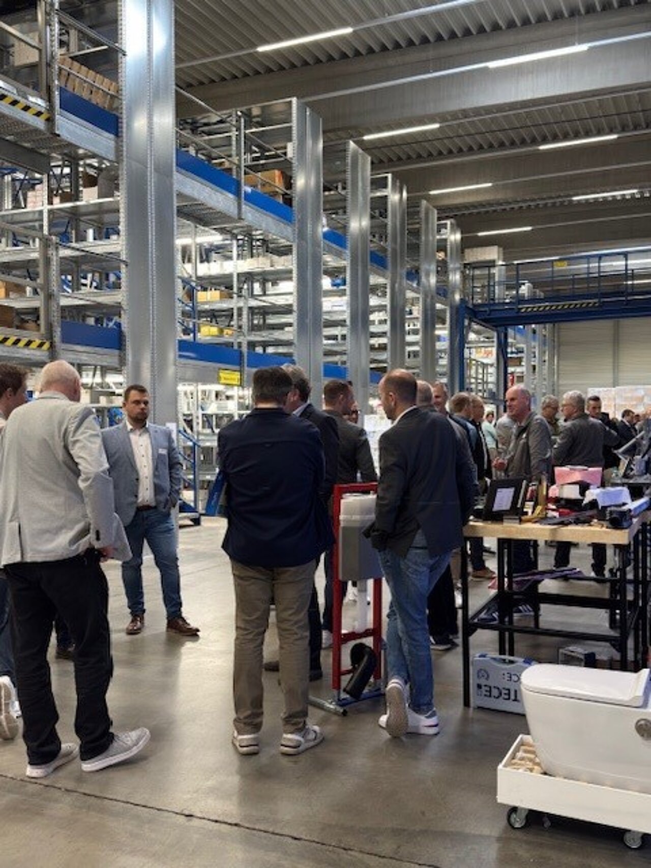 Eine Gruppe von Menschen in Geschäftskleidung versammelt sich in einer großen Lagerhalle.