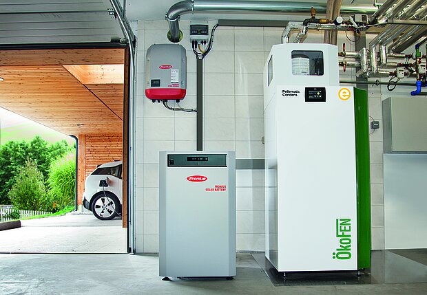Ein moderner Hauswirtschaftsraum mit einem weißen ÖkoFEN-Heizkessel und einer roten und grauen Solarbatterie.