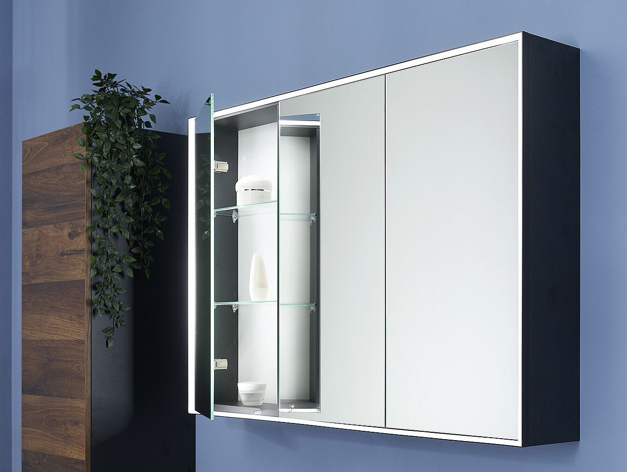 Ein wandmontierter Badezimmerschrank mit Spiegeltüren, von denen eine Tür geöffnet ist.