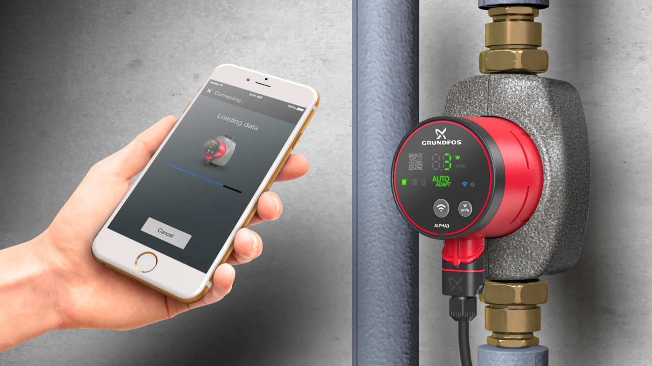 Eine Hand hält ein Smartphone, auf dem ein Datenladebildschirm neben einer roten Grundfos-Pumpe.