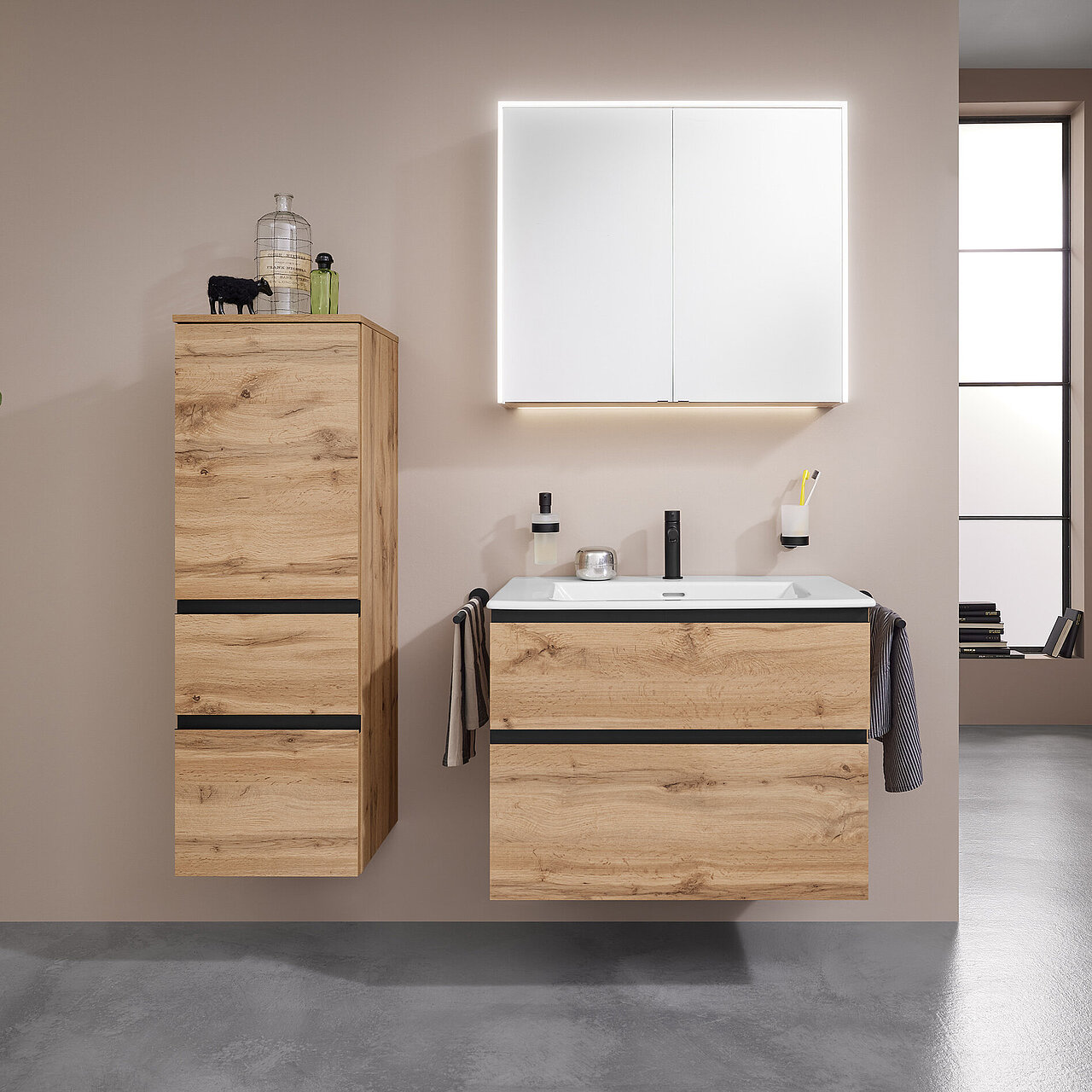 Modernes Bad mit schwebenden Schränken aus hellem Holz, einem weißen Waschbecken, einem Spiegelschrank mit Hintergrundbeleuchtung und einer schwarzen Wandtoilette.