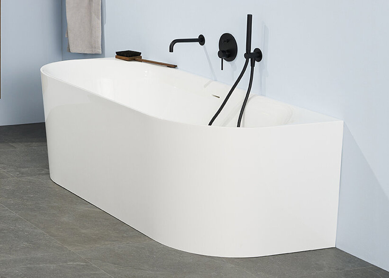 Eine moderne, weiße Badewanne mit schwarzen Armaturen steht an einer hellblauen Wand