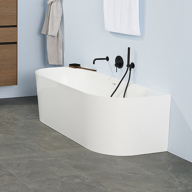 Eine moderne, weiße Badewanne mit schwarzen Armaturen steht an einer hellblauen Wand