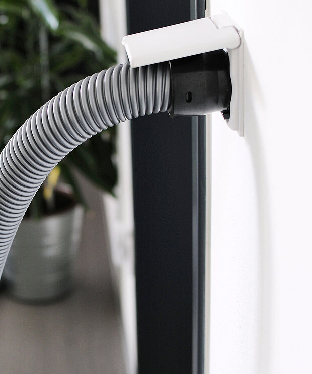 Grauer flexibler Schlauch in weißer Wandsteckdose, der Anschluss eines Zentralstaubsaugers.