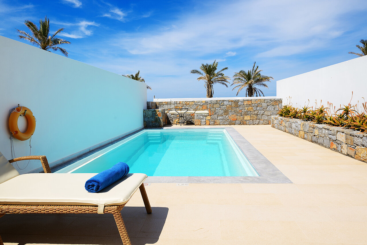 Ein privater Swimmingpool mit klarem, blauem Wasser, umgeben von weißen Wänden und steinernen Akzenten.