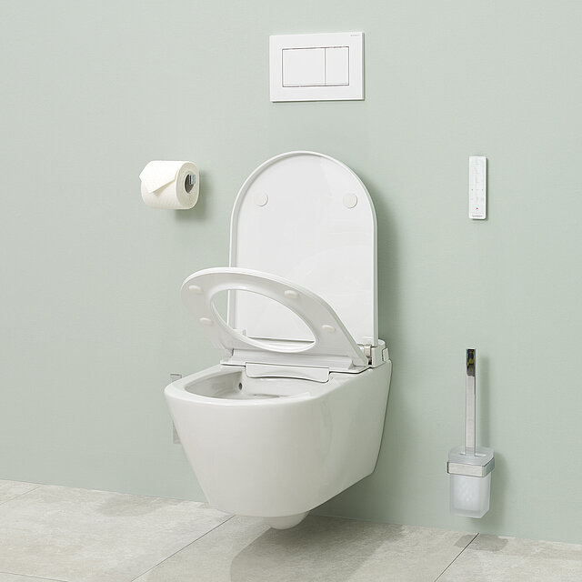 Ein modernes Dusch-WC mit offenem Deckel, einer Toilettenbürste, einem wandmontierten Toilettenpapierhalter mit Rolle und einer Spülplatte