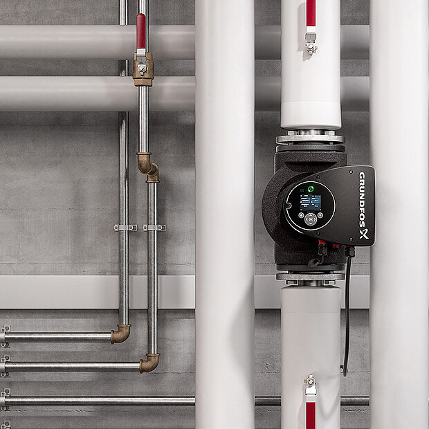 Grundfos-Umwälzpumpe installiert zwischen zwei großen weißen Rohren, umgeben von Metallleitungen vor Betonwand.