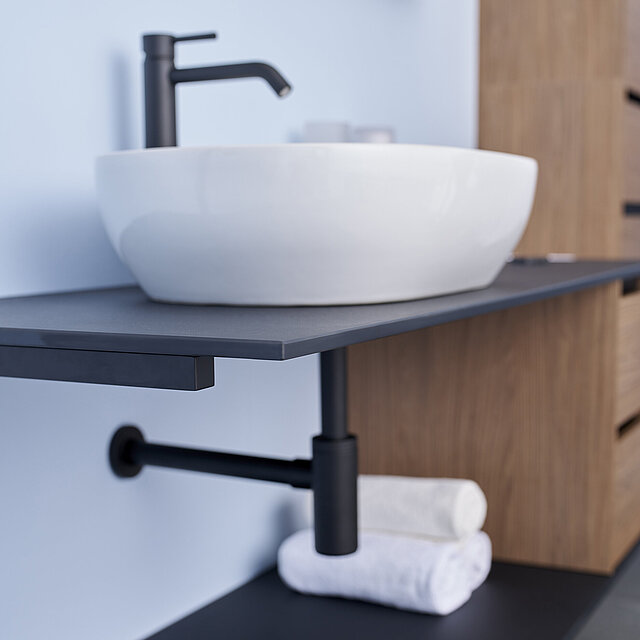 Ein modernes Waschbecken mit weißem Gefäß und mattschwarzem Wasserhahn auf einer schwebenden dunklen Arbeitsplatte.