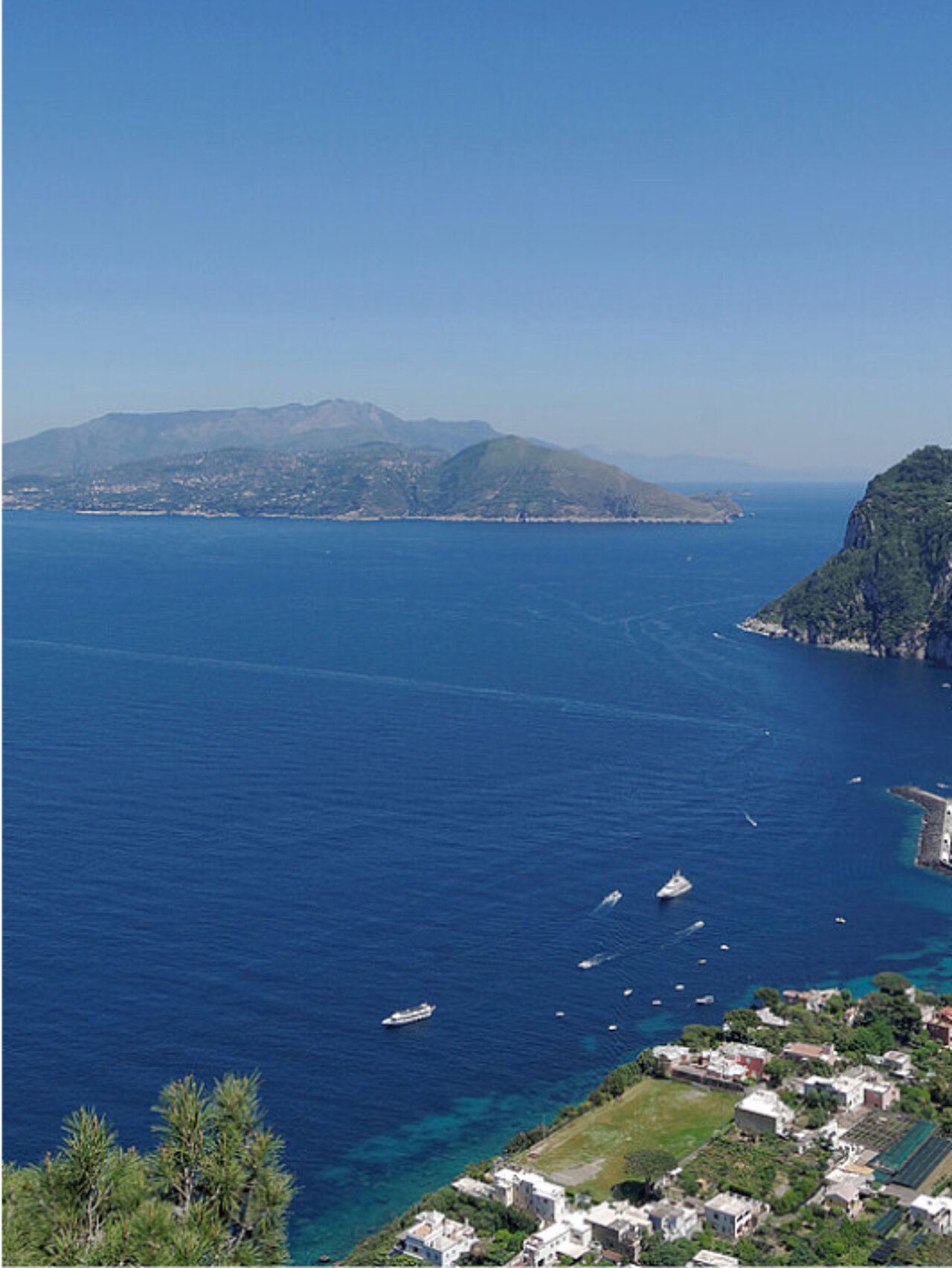 Eine Küstenansicht mit tiefblauem Meer, mehreren Booten, einer grünen bergigen Insel.