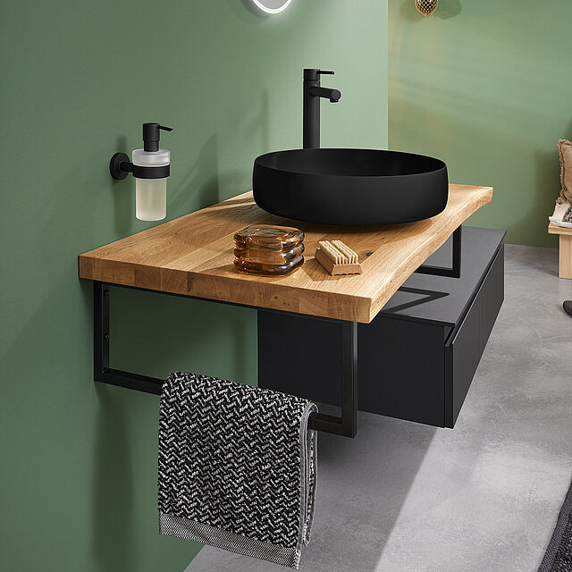 Modernes Bad mit einer hölzernen Arbeitsplatte, einem schwarzen Waschbecken, runden Spiegel und schwarzen Armaturen.