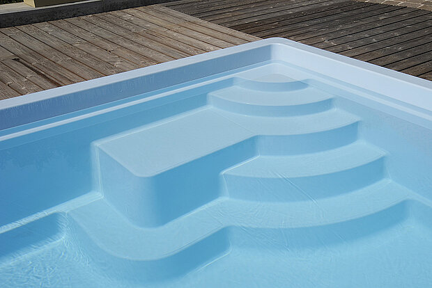 Nahaufnahme eines modernen Swimmingpools mit eingebauten Stufen und einer Sitzgelegenheit neben einem Holzdeck.