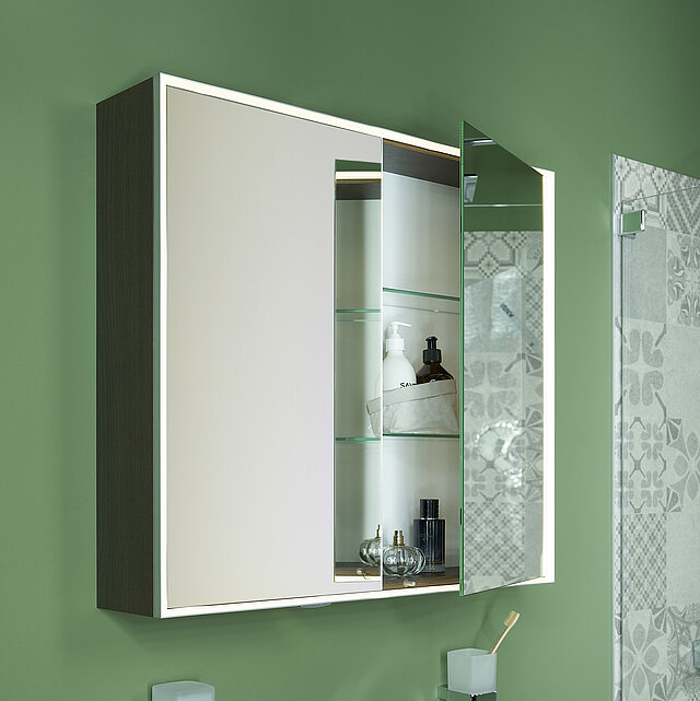 Modernes Bad mit einem weißen Waschbecken und einem Spiegelschrank mit Glasfächern. Die Schranktür ist leicht geöffnet..