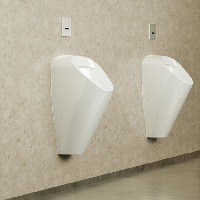 Zwei moderne weiße Wandurinale mit schlichtem, kantigem Design sind nebeneinander an einer hellbeige gefliesten Wand installiert.