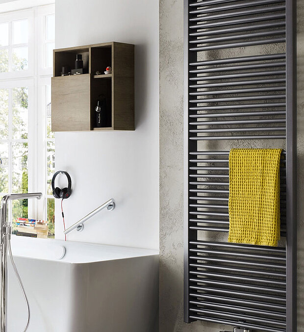 Badezimmer mit einem hohen schwarzen Handtuchheizkörper, an dem ein gelbes Handtuch hängt. 