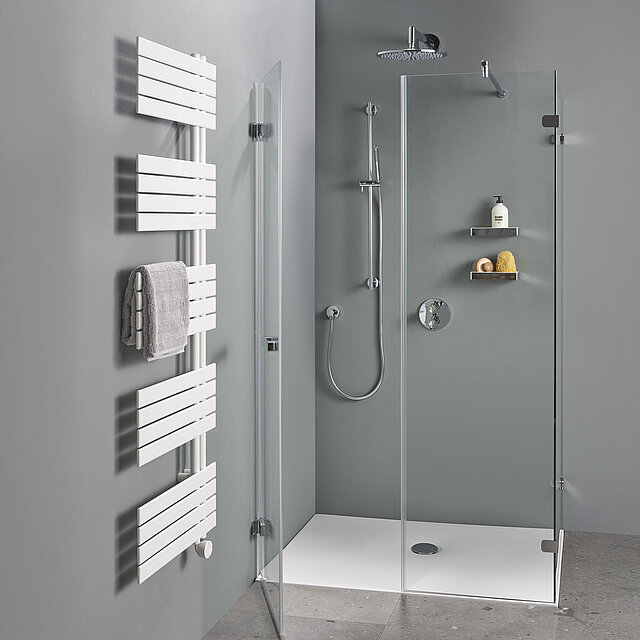 Modernes Badezimmer mit begehbarer Glasdusche, Kopf- und Handbrause, weißem Handtuchwärmer mit grauem Handtuch und grauen Wänden und Fußböden.