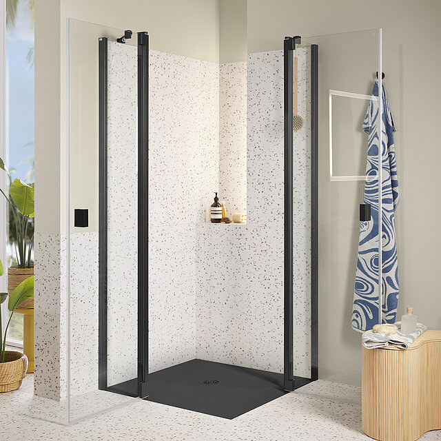 Eine moderne Dusche mit Glastüren, schwarzem Rahmen, Wänden im Terrazzo-Stil und einem eingebauten Regal.