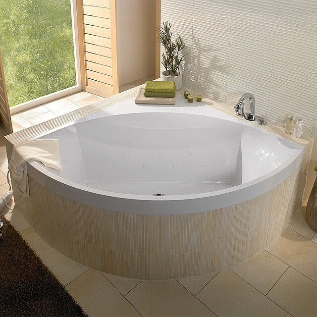 Eine moderne, weiße Eckbadewanne in einem hellen Badezimmer mit beige gefliesten Wänden und Böden